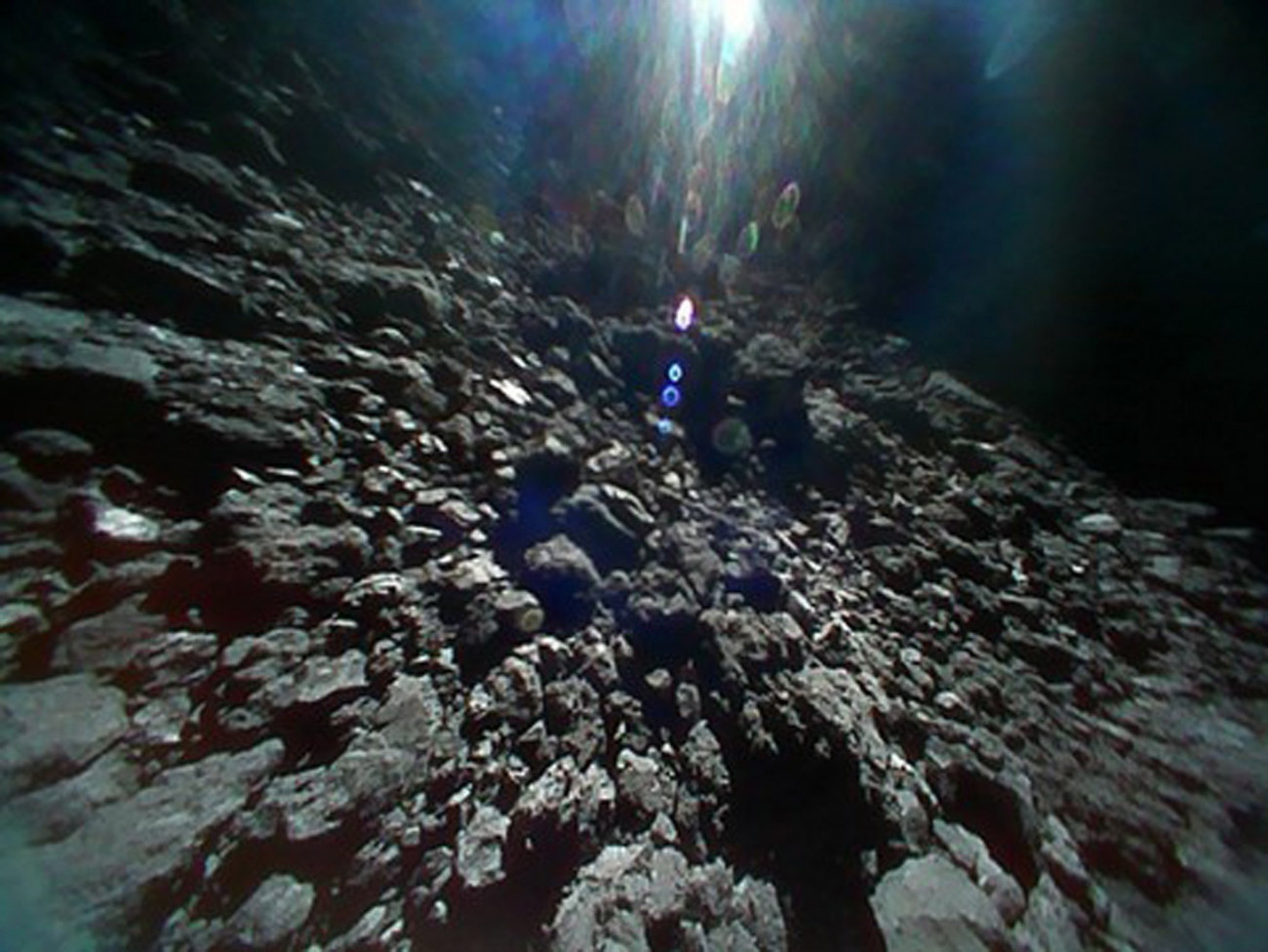 Világűr, 2018. szeptember 28.
A JAXA japán űrügynökség felvétele a Ryugu nevű kisbolygó felszínéről 2018. szeptember 23-án. A felvételt a Hajabusza-2 (Sólyom-2) aszteroidavizsgáló űrszondáról levált, Minerva-2 nevű, robotvezérlésű Rover1B kutatóműszer készítette. A 2014-ben útnak indított Hajabusza-2 űrszonda 2018. június 27-én érte el a Földtől mintegy 280 millió kilométerre levő, egy kilométer átmérőjű Ryugu aszteroidát. A kutatóroverek feladata, hogy felvételeket készítsenek az aszteroidáról, megmérjék a felszíni hőmérsékletét. A csillagászok szerint a Ryugu a Naprendszer hajnalán formálódhatott, így feltételezéseik szerint olyan szerves anyagokat tartalmazhat, amelyek a földi élet kialakulásához is hozzájárulhattak. (MTI/EPA/JAXA)