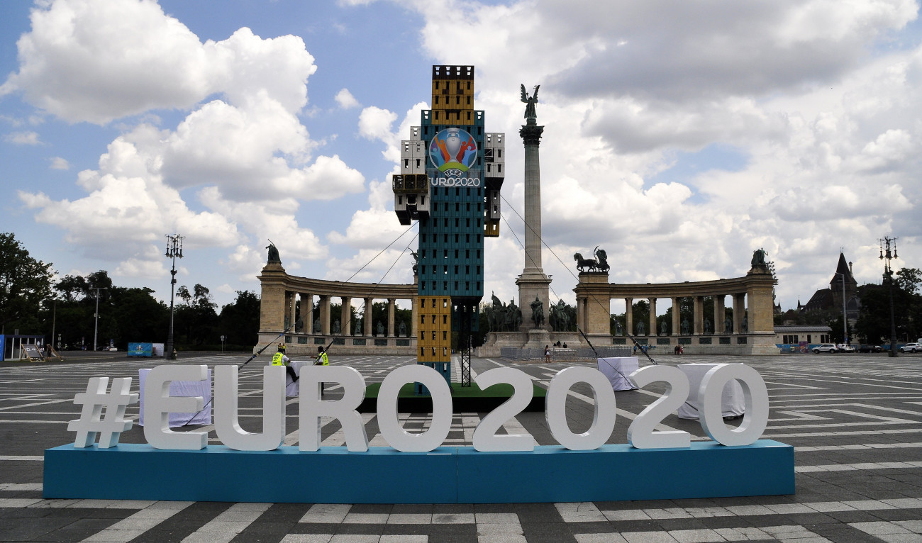 Budapest, 2021. június 11.
Sörös ládákból készített, labdarúgót ábrázoló dekoráció a Hősök terén a Millenniumi emlékmű előtt a Labdarúgó Európa-bajnokság szurkoló zónájában. A 2020-as labdarúgó Európa-bajnokságot, az Euro 2020-at, ami a 16. Európa-bajnokság, Európa-szerte 11 városban rendezik meg, s amelyre eredetileg 2020. június 12. és július 12. között került volna sor, de a koronavírus-járvány miatt elhalasztották. A mérkőzéseket 2021. június 11. és július 11. között rendezik meg és hazánkban a budapesti Puskás Arénában lesznek a találkozók. A Városligetben három Szurkolói Zóna várja a rajongókat: óriáskivetítőkkel készül a Hősök tere, az Olof Palme sétány mentén Futballfalu, a Városligeti Műjégpálya és Csónakázótó vizén pedig egy VIP lounge került kialakításra.
MTVA/Bizományosi: Balaton József