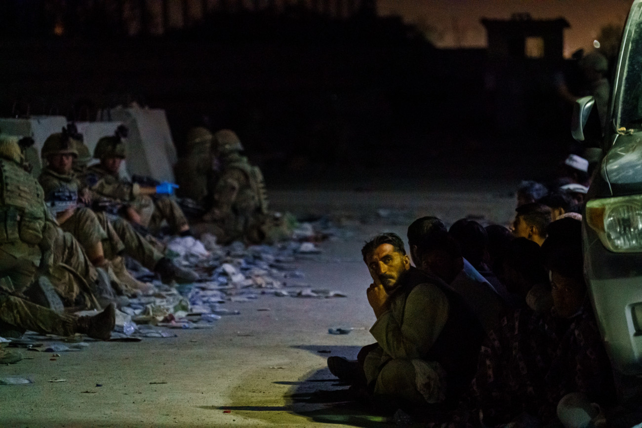 KABUL, AFGHANISTAN -- AUGUST 26, 2021: Afghan refugees crouch in a group as British military secure the perimeter outside the Baron Hotel, near the Abbey Gate, in Kabul, Afghanistan, Thursday, Aug. 26, 2021. (MARCUS YAM / LOS ANGELES TIMES)