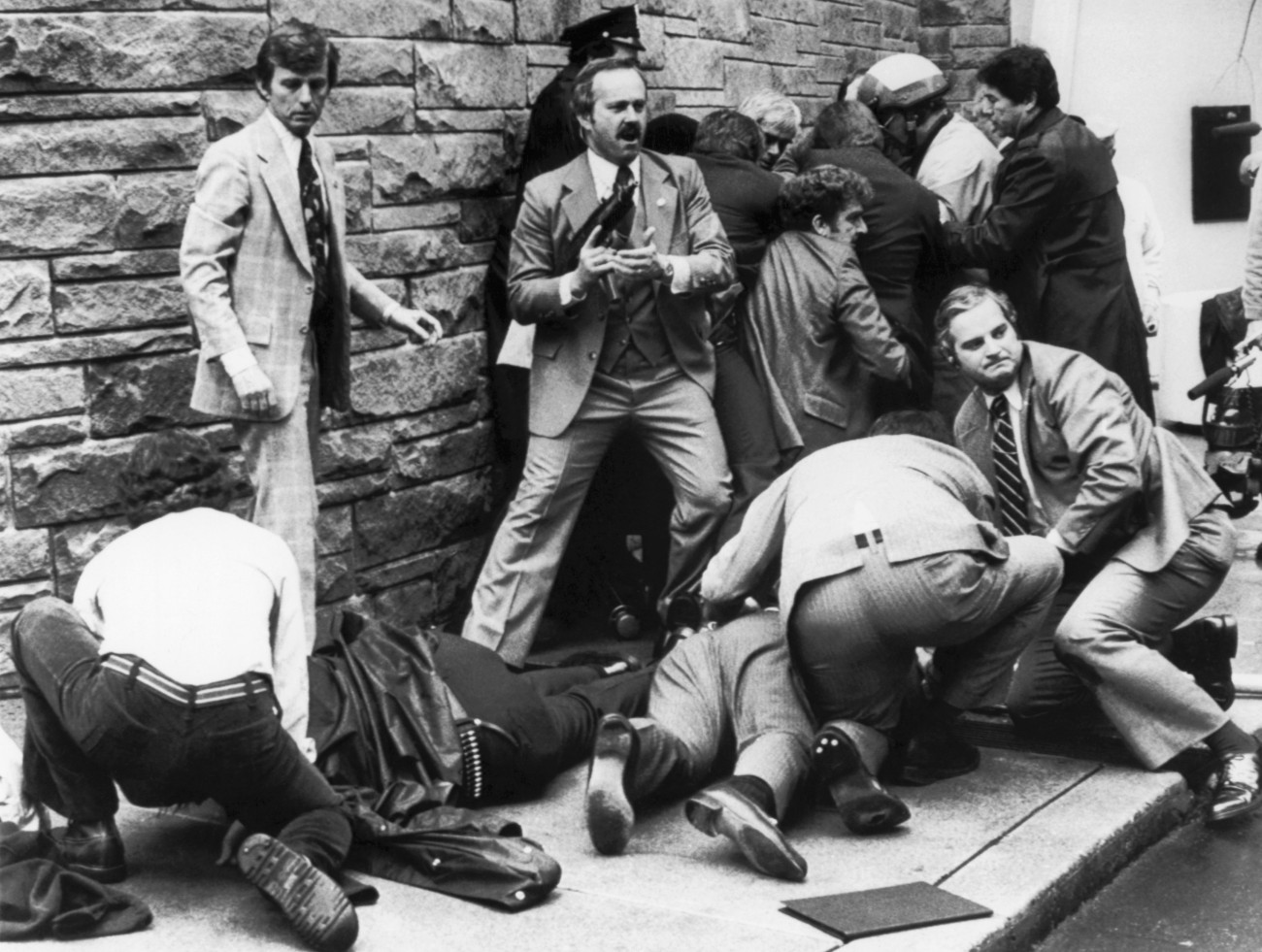 Secret Service agents, police officers, and bystanders take action seconds after shots were fired at President Reagan and his retinue by John Hinckley, Jr. The group in the background apprehended and disarmed Hinckley, while those in the foreground tended to the seriously wounded, who included Press Secretary James Brady. President Reagan, himself wounded, was hurried into his waiting car and taken to the hospital.