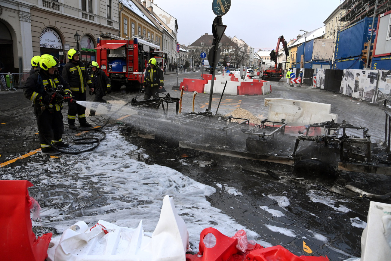 Budapest, 2023. december 11.
Kiégett elektromos városnéző kisbusz oltásának utómunkálatain dolgoznak tűzoltók a főváros I. kerületében, a budavári Dísz téren 2023. december 11-én.
MTI/Mihádák Zoltán