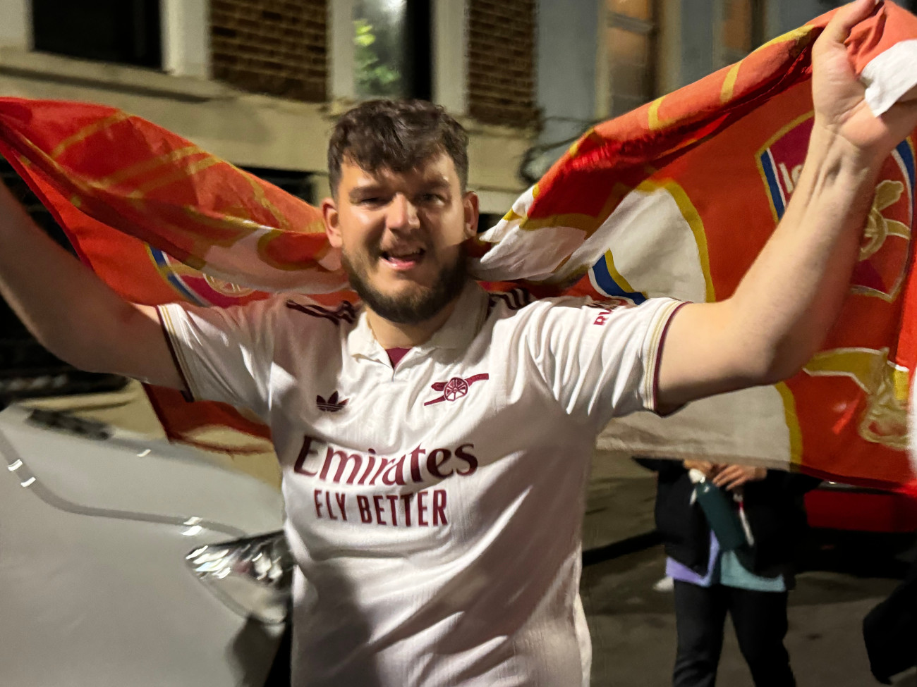 Egy Arsenal-szurkoló, hátán a csapat zászlajával a Premier League bajnoki címének elnyerését követő utcai ünneplésen, 2026. május 19-én. (Fotó: Szvetnik Endre, London)