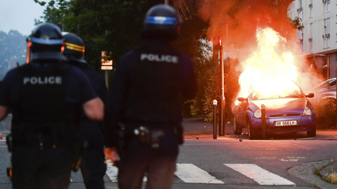 Nantes, 2018. július 4.Felgyújtott autó lángol rendőrök közelében a nyugat-franciaországi Nantes Breil nevű városrészében 2018. július 3-án, miután zavargás tört ki amiatt, hogy a rendőrség lelőtt egy igazoltatásnak ellenálló férfit. Az incidenst követően helyi fiatalok gépkocsikat és épületeket gyújtottak fel három elővárosi negyedben. A 22 éves Aboubakar F. egy kábítószer-kereskedelemmel kapcsolatos nyomozás okán keresett gépkocsival próbált elmenekülni az igazoltatás helyszínéről, amikor a nyakán eltalálták, és a kórházba szállítása közben belehalt sérülésébe. (MTI/AP/Franck Dubray)