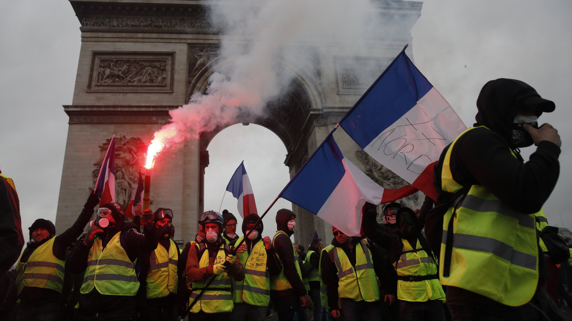 Jelzőfáklyákkal a kezükben vonulnak a dráguló üzemanyagárak ellen tiltakozó sárga láthatósági mellényt viselő tüntetők a Diadalív előtt a párizsi Champs-Elysées sugárúton 2018. december 1-jén.