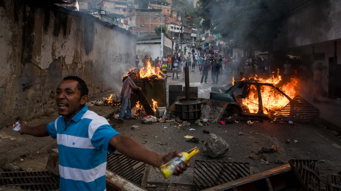 Tüntetők által emelt útakadály ég a nemzeti gárdisták egyik laktanyája közelében Caracasban 2019. január 21-én. A venezuelai különleges egységek a nap folyamán körülzárták a laktanyát, miután több nemzeti gárdista is megtagadta az engedelmességet a heves nemzetközi tiltakozások ellenére január 10-én beiktatott szocialista Nicolás Maduro elnöktől. A zendülők feladták magukat.