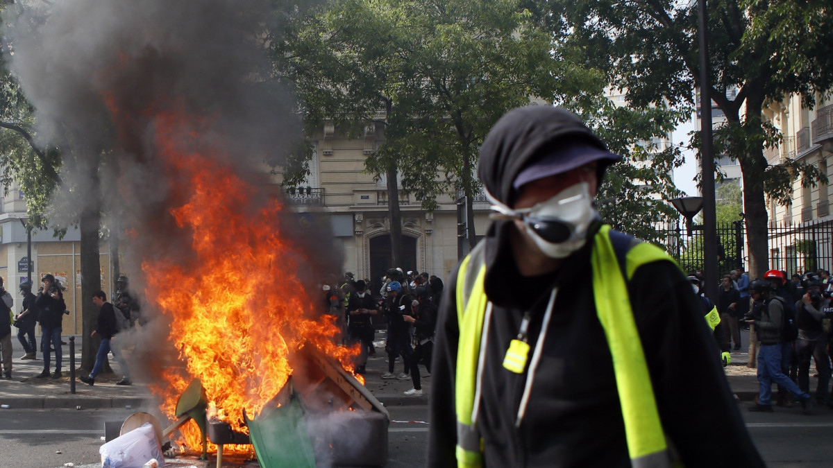 Felgyújtott kuka mellett egy tiltakozó, miközben a munka ünnepének alkalmából tartott tüntetés radikális résztvevői összecsapnak a rohamrendőrökkel Párizsban 2019. május 1-jén.