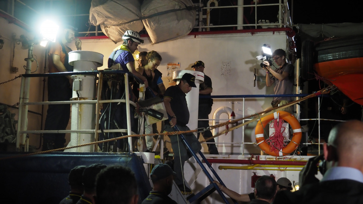 A Sea-Watch nevű német nem kormányzati szervezet által közreadott képen Carola Racketét, a szervezet Sea Watch 3 nevű holland bejegyzésű hajójának kapitányát (k) őrizetbe veszik Lampedusán 2019. június 29-én, miután a 43, Európába igyekvő illegális bevándorlót szállító hajó kikötési engedély nélkül, erőszakkal a kikötőbe hajtott. Az olasz hatóságok hajói megpróbálták feltartóztatni, de a Sea Watch 3 az egyiknek majdnem nekiment és a dokknak szorította.