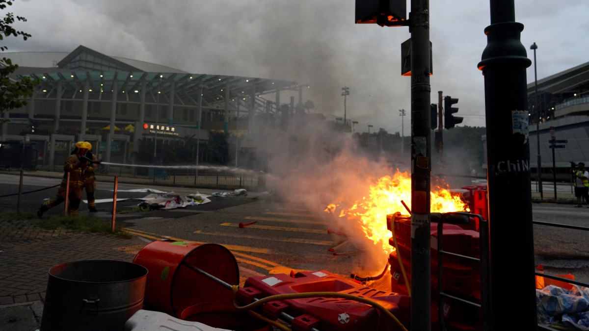 Demokráciapárti tüntetők által felgyújtott útakadályt locsolnak tűzoltók a hongkongi repülőtér közelében levő Tung Chung vasútállomásnál 2019. szeptember 1-jén. A hongkongi vasúti társaság a kormányzat és a reptéri hatóságok kérésére leállította a repülőtérre vezető vasúton a forgalmat.