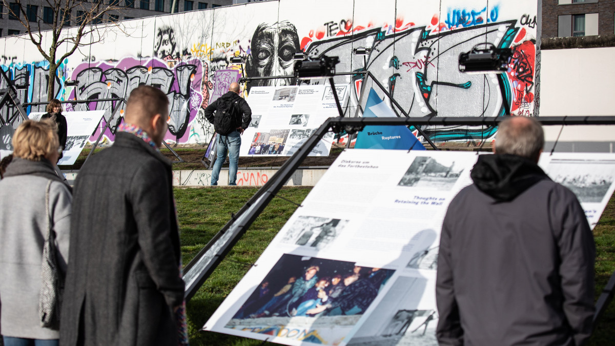 Látogatók nézik az információs táblát a berlini fal Keleti Oldali Galéria (East Side Gallery) nevű szakaszánál 2019. november 4-én,  öt nappal a berlini fal ledöntésének 30. évfordulója előtt.