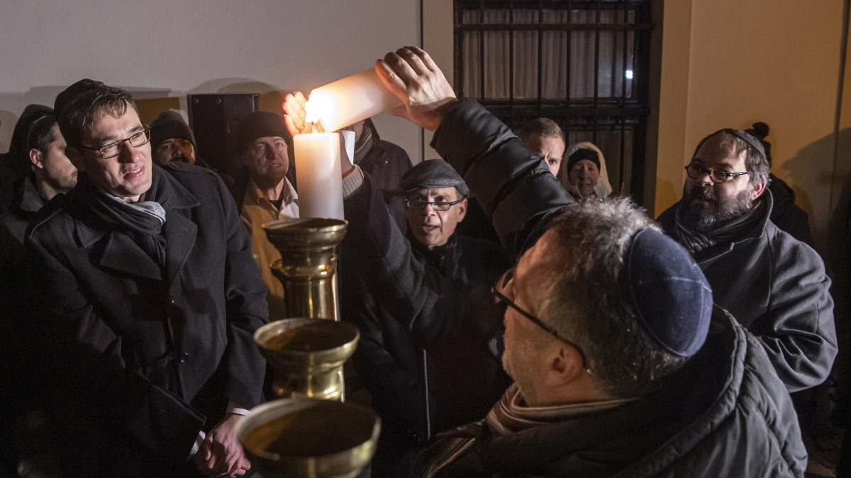 Heisler András, a Magyarországi Zsidó Hitközségek Szövetsége (Mazsihisz) elnöke (előtérben) meggyújtja a gyertyát, szemben Karácsony Gergely főpolgármester (b), Jákov Hadasz-Handelszman kijelölt izraeli nagykövet (k), Radnóti Zoltán neológ főrabbi (j) a nyolcnapos zsidó vallási ünnep, a hanuka második estéjén, a Budavári Önkormányzat és a Mazsihisz ünnepségén, a második hanukagyertya meggyújtásán a hanukián, a kilencágú gyertyatartón a budai Várban, az eltemetett zsinagóga emléktáblájánál 2019. december 23-án.