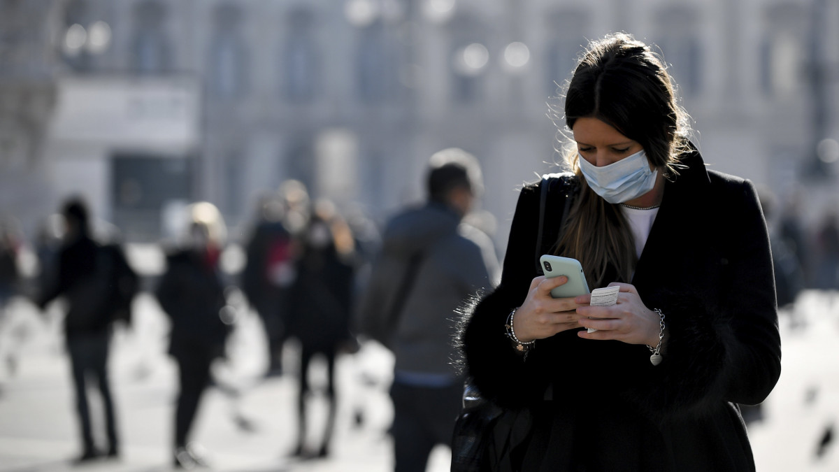 Egészségügyi maszkot viselő járókelő a telefonját használja Milánóban 2020. február 24-én. Az osztrák hatóságok az előző nap felfüggesztették a vasúti átkelést az Olaszországgal közös határon, miután a Velencéből induló, Münchenbe tartó nemzetközi  járatok egyikén az új koronavírus fertőzés tüneteit állapították meg két utasnál. Olaszországban 160-ra emelkedett a tüdőgyulladást okozó vírussal fertőzöttek száma, és hatan veszítették életüket. A halálos áldozatok mindannyian idős, más betegségben is szenvedő emberek voltak.