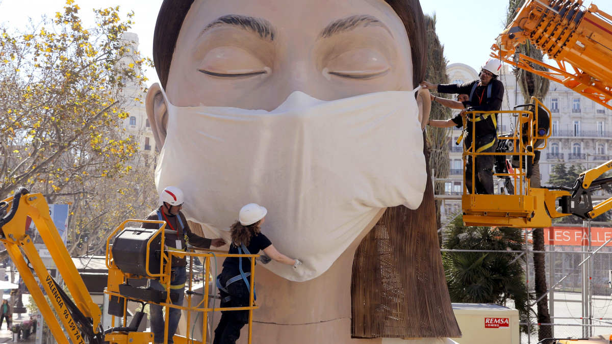 Munkások egy hatalmas maszkot helyeznek az egyik papírbábura a kelet-spanyolországi Valenciában 2020. március 11-én, két nappal a Szent József napján tartott Fallas Fesztivál előtt. A szervezők a koronavírusos fertőzés miatt lefújták a rendezvényt.