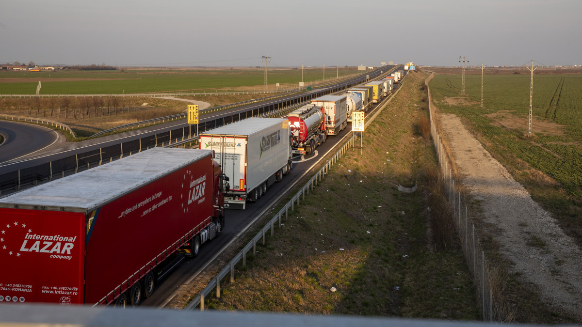 Kamionok várakoznak a csanádpalotai magyar-román autópálya-határátkelőhely közelében, az M43-as autópályán 2020. március 20-án. Ezen a napon tizenkét órásra nőtt a kamionok várakozási ideje, a várakozásra kényszerülő árufuvarozóknak a rendőrök és a katasztrófavédelem munkatársai vizet osztanak. Több mint 35 kilométeres kamionsor alakult ki a Romániába tartó tehergépjárművekből.