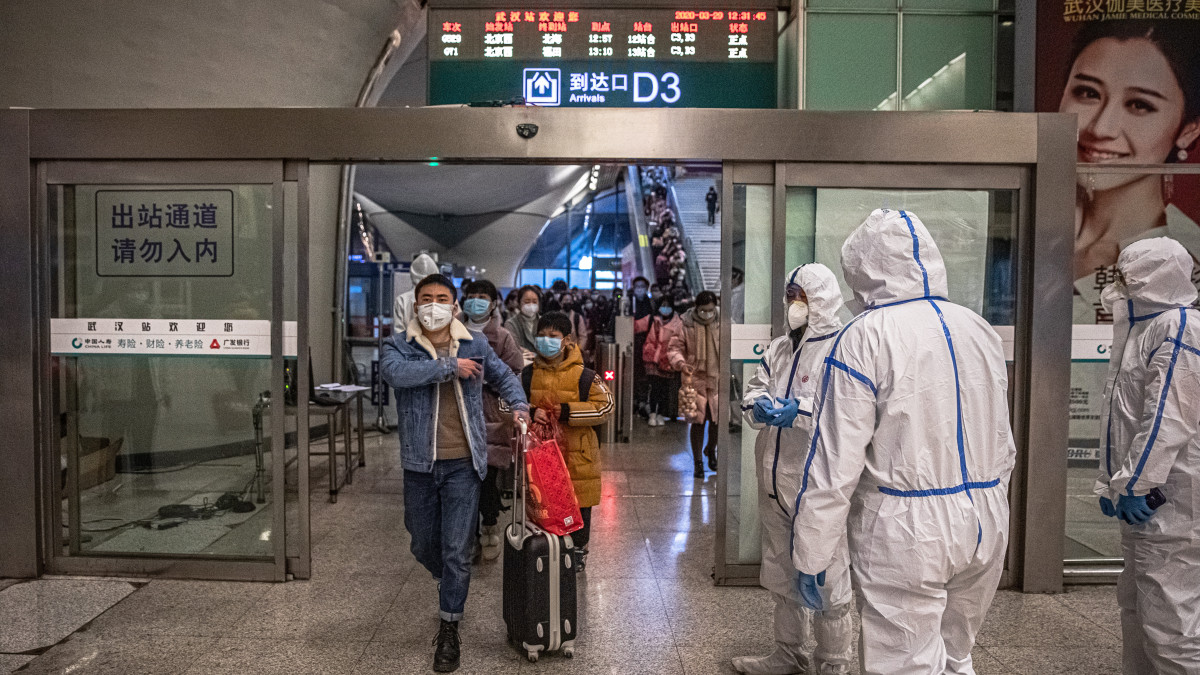 Vuhan, 2020. március 29.Utasok és védőöltözetet viselő dolgozók egy vuhani pályaudvaron 2020. március 29-én. A hatóságok részlegesen újraindították a tömegközlekedést a koronavírus-járvány eredeti gócpontjának számító kínai nagyvárosban.