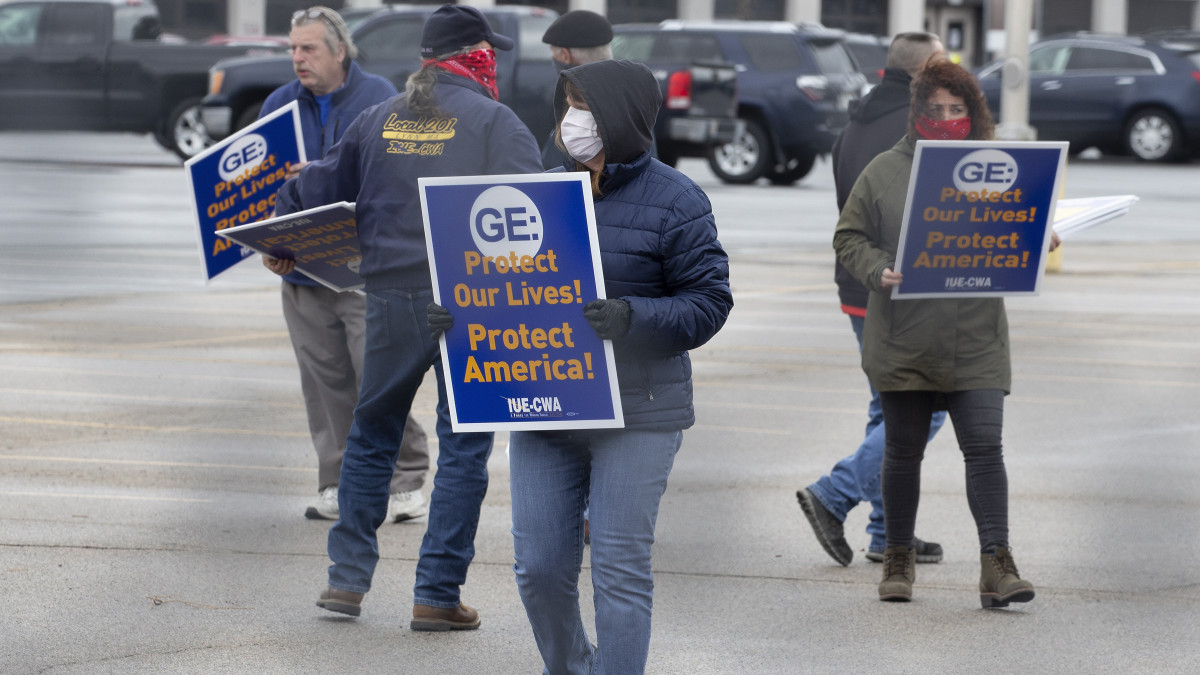 Védd meg az életünket! Védd meg Amerikát! feliratú táblával a kezükben tüntetnek egy ipari munkásokat tömörítő amerikai szakszervezet (IUE-CWA) tagjai a General Electric (GE) multinacionális vállalat üzeménél a Massachusetts állambeli Lynn településen 2020. április 9-én. A koronavírus-járvány miatt a szakszervezet követeli, hogy a GE minél hamarabb kezdjen el lélegeztetőgépeket gyártani, valamint szerezzen be a munkások testhőmérsékletének mérésére alkalmas eszközöket.