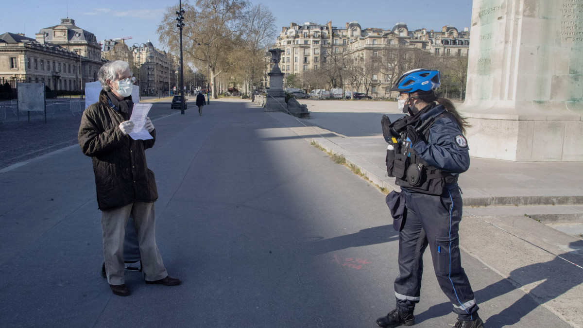 Védőmaszkos járókelő papírjait ellenőrzi biztonságos távolságról egy szintén védőmaszkos rendőrnő Párizsban a koronavírus-járvány idején, 2020. április 6-án. A járvány miatt a francia kormány meghosszabbította a március 17-én életbe léptetett kijárási korlátozásokat az országban.