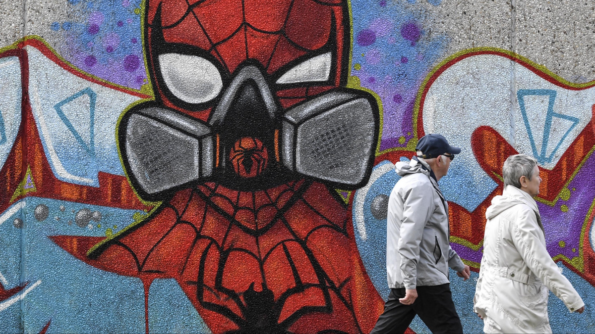 Két ember halad el egy légzőmaszkos Pókembert ábrázoló, az Uzey néven ismert utcaművész által készített graffiti előtt a koronavírus-járvány idején a németországi Hamm városában 2020. április 13-án.