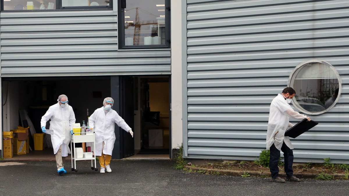 Védőruhát viselő egészségügyi dolgozók teszteléshez készülődnek a délnyugat-franciaországi Anglet város biológiai laboratóriuma előtt létesített autós tesztállomáson 2020. április 20-án, a koronavírus-járvány idején.