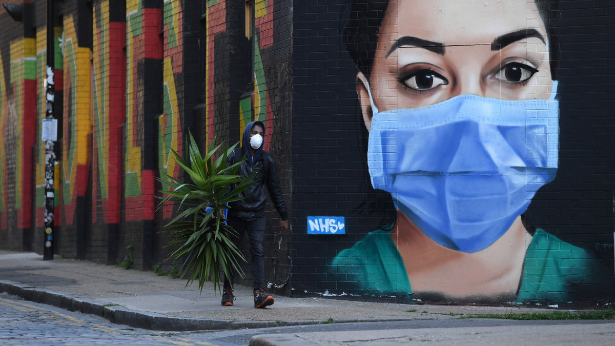 Egy férfi halad el egy védőmaszkot viselő ápolónőt ábrázoló falfestmény előtt Londonban 2020. április 22-én. A koronavírus-járvány miatt Nagy-Britanniában kijárási korlátozások vannak érvényben.