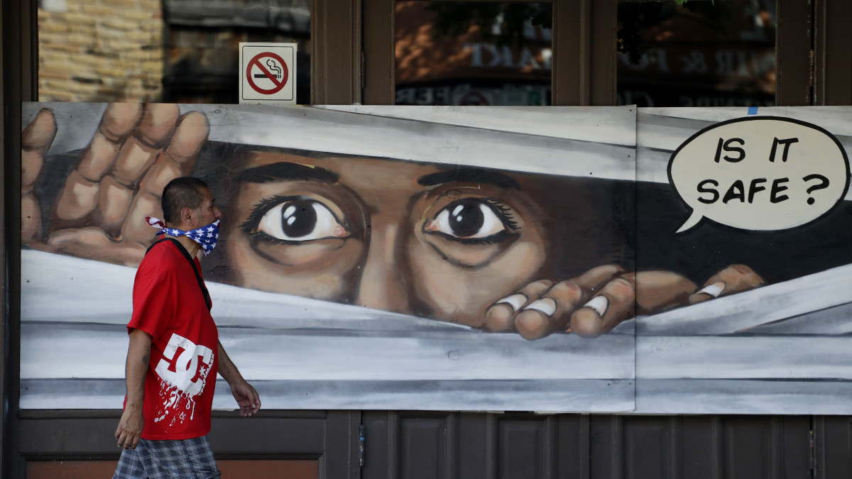 A koronavírus-járvány miatt az arcát kendővel elfedő férfi halad el egy bezárt üzlet falára festett festmény előtt a Texas állambeli Austinban 2020. április 27-én. Greg Abbott, Texas kormányzója bejelentette, hogy enyhíti a járvány miatt bevezetett, a gazdaságot érintő korlátozások egy részét.
