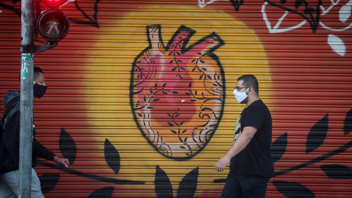 Védőmaszkot viselő férfi halad el egy falfestmény előtt a brazíliai Sao Paulo egyik metróállomása közelében 2020. május 4-én. A koronavírus-járvány terjedésének megfékezése érdekében ettől a naptól kötelező maszkot viselni a tömegközlekedési eszközökön a városban.