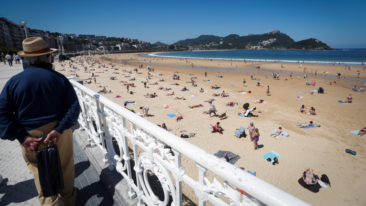 Egymástól biztonságos távolságra napfürdőznek az emberek a baszkföldi San Sebastián város La Concha tengerpartján 2020. május 27-én, a koronavírus-járvány idején.