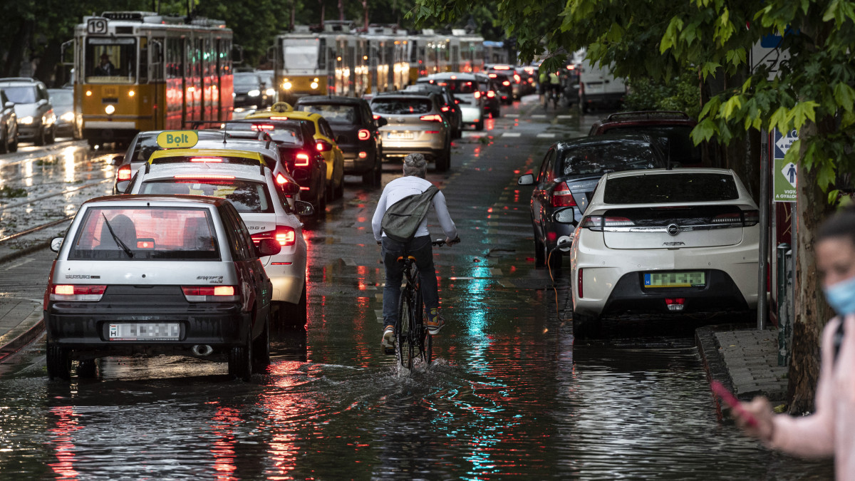 Kerékpáros, valamint autók és villamosok az esővízzel elöntött Bartók Béla úton a főváros XI. kerületében a vihar után 2020. június 17-én.