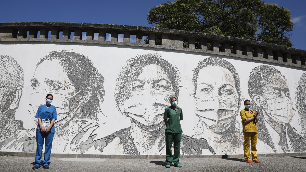 Raquel Queiros, Maria Joao és Idalina Ramos egészségügyi dolgozók (b-j) az őket ábrázoló portrék előtt, a portugáliai Portóban 2020. június 19-én. A VHILS művésznéven alkotó Alexandre Farto graffitikészítő tíz egészségügyi dolgozó portréját festette meg a Sao Joao Kórház falára, az irántuk érzett tisztelete és hálája jeléül, amiért erejüket megfeszítve gyógyítják a koronavírus-járvány betegeit.