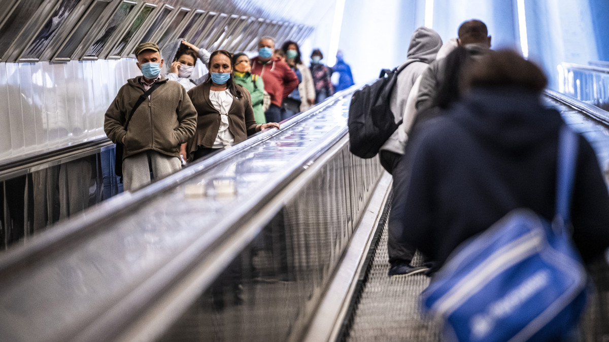 Védőmaszkot viselő utasok a Széll Kálmán téri metróálllomás mozgólépcsőjén 2020. április 27-én. Ettől a naptól csak sállal, kendővel vagy maszkkal eltakart arccal szabad felszállni a fővárosi tömegközlekedés járataira, s így lehet csak boltba menni és taxival utazni a koronavírus-járvány terjedésének megakadályozása érdekében. Az intézkedés nem vonatkozik a 6 éven aluli utasokra. A rendelkezés betartásának elősegítése érdekében a Budapesti Közlekedési Központ (BKK) és a Főpolgármesteri Hivatal több csomópontban mosható és vasalható textilmaszkot oszt az utazóknak.