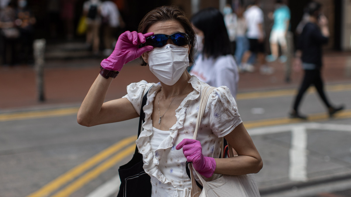 Védőmaszkot és gumikesztyűt viselő nő Hongkong belvárosában 2020. július 27-én. A koronavírus-járvány újabb hulláma, az új esetek számának gyors emelkedése miatt Hongkongban kötelezővé tették a maszk viselését a közterületeken. Július 29-étől a hatóságok betiltják a két fősnél nagyobb létszámú nyilvános találkozókat, az éttermek pedig csak elvitelre szolgálhatnak ki. Az intézkedések egyelőre hét napig lesznek érvényben.