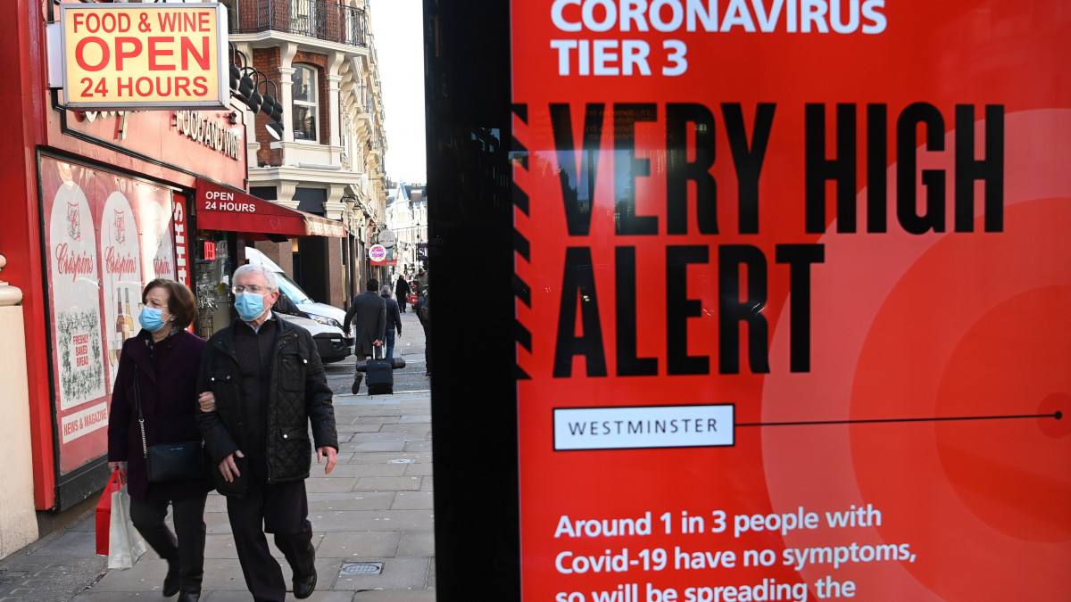 A koronavírus-járvány miatt védőmaszkot viselő emberek a járványügyi szabályokra figyelmeztető felhívás mellett haladnak el Londonban 2020. december 17-én. Matt Hancock brit egészségügyi miniszter bejelentette, hogy Dél-Anglia újabb kiterjedt térségei kerülnek a hétvégétől a koronavírus-járvány megfékezésére kidolgozott háromfokozatú készenléti rendszer legmagasabb szintjének hatálya alá. Ez azt jelenti, hogy be kell zárniuk a múzeumoknak, a turistalátványosságoknak, a zárt terű szórakozóhelyeknek, a szállodáknak, valamint az összes vendéglátóhelynek.