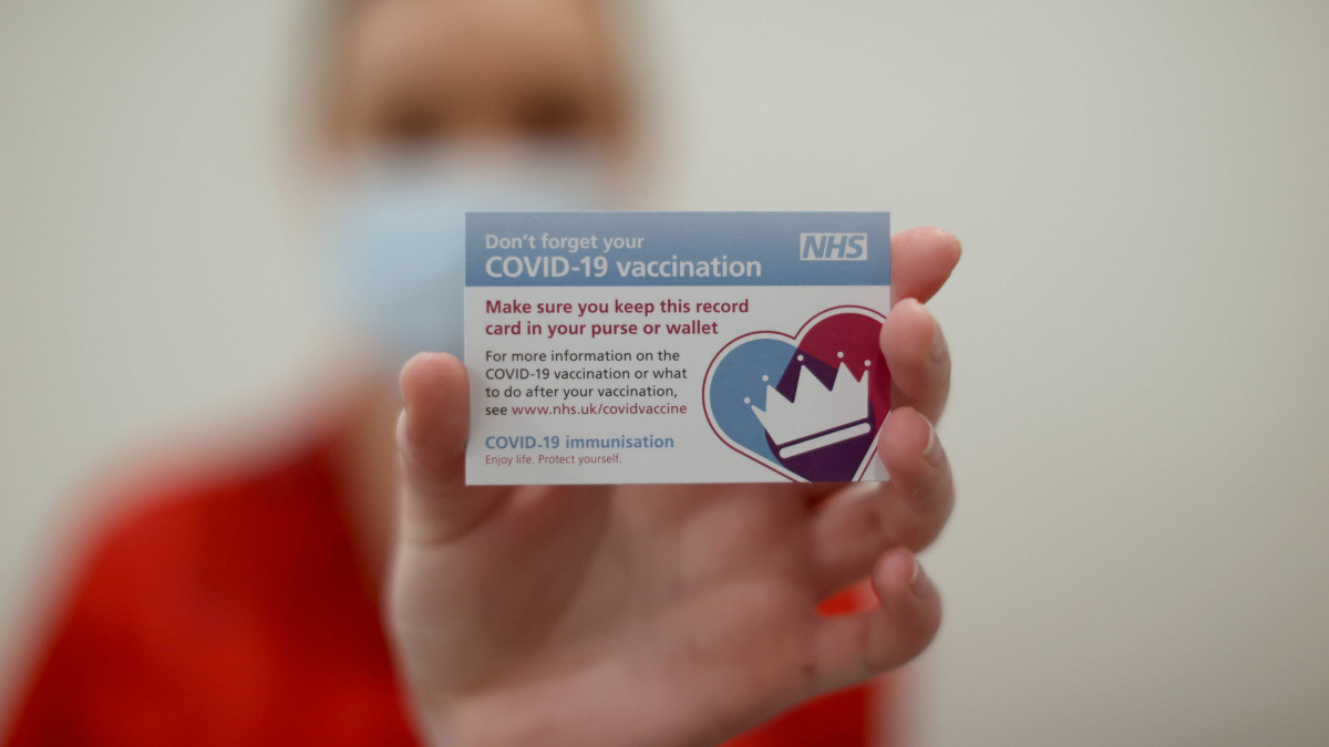 A koronavírus-járvány elleni oltás beadását igazoló kártyát tarja kezében egy ember a belfasti Royal Victoria Kórházban 2020. decemberi 8-án. Az Egyesült Királyságban megkezdték az új típusú koronavírus elleni tömeges oltási kampányt, amelynek során a Pfizer-BioNTech oltóanyagkifejlesztő vállalatok koronavírus elleni vakcinájával oltják be a veszélyeztetett munkakörökben dolgozó és a 80 évnél idősebb embereket.