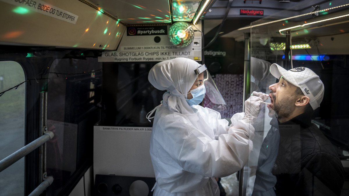 Egészségügyi dolgozó mintát vesz egy férfitől koronavírus-teszthez egy mobil koronavírus-tesztállomáson a dániai Ishoejben 2021. február 23-án. Mintavétel közben a páciensek zenét hallgathatnak a villogó fényekkel megvilágított buszban.