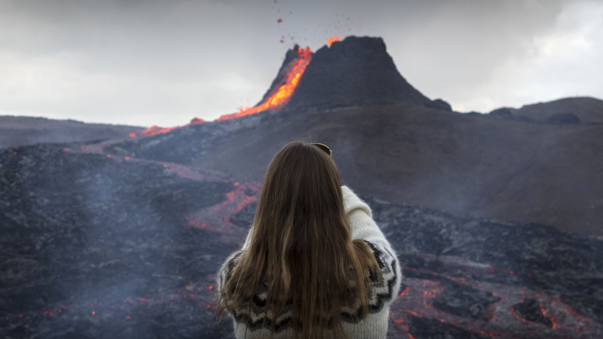 Egy nő fényképezi, ahogy izzó lávafolyam ömlik egy vulkán kráteréből az izlandi fővárostól 30 kilométerre délnyugatra, a Reykjanes-félszigeten 2021. március 23-án. A szigetnek ezen a részén utoljára 800 éve fordult elő vulkánkitörés.