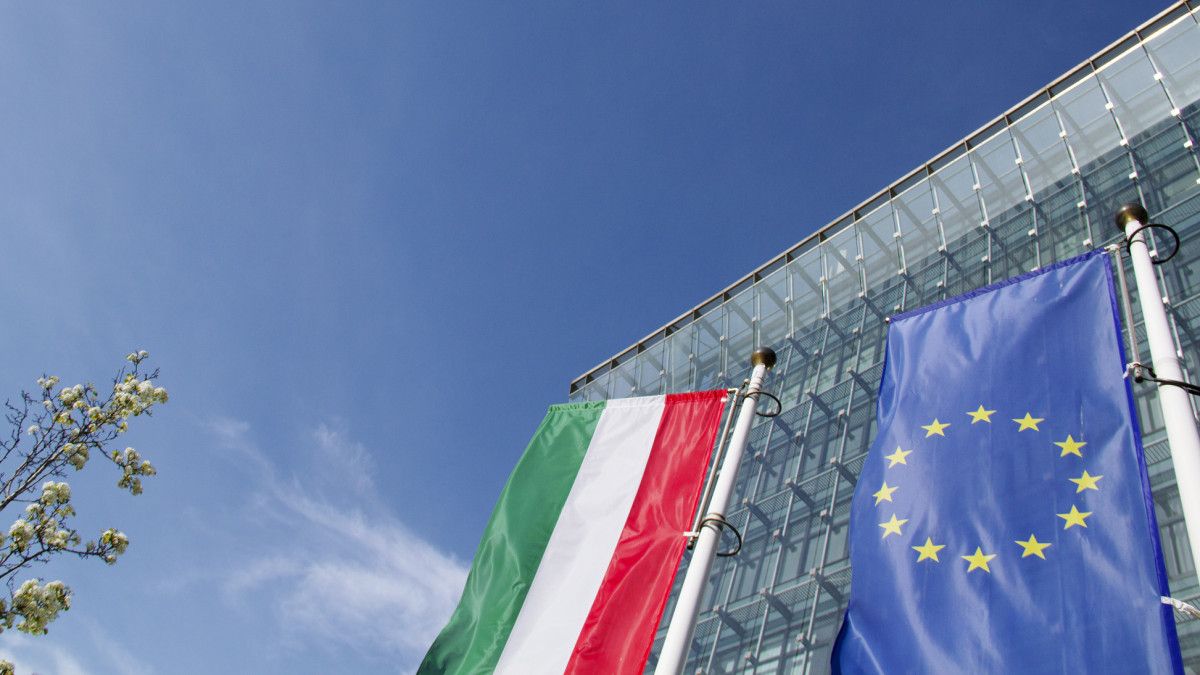 Financial Building Reflecting with Sunshine and Blue Sky, Springtime Tree, Flag of Hungary and European Union Flag in the Foreground in Kalvin Square, 8th District of Budapest Downtown, Hungary in April 2021