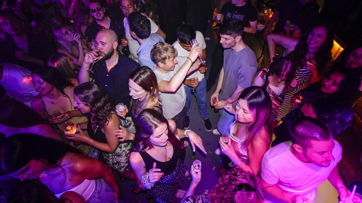 Szórakozó fiatalok a londoni Farringdon kerületben lévő The Piano Works bárban a 2021. július 19-re virradó éjszaka. Ezen a napon megszűnt a járvány terjedésének megfékezésére bevezetett utolsó jogi korlátozások zöme Angliában, így kinyithattak a 2020 márciusa óta zárva tartó éjszakai szórakozóhelyek is.