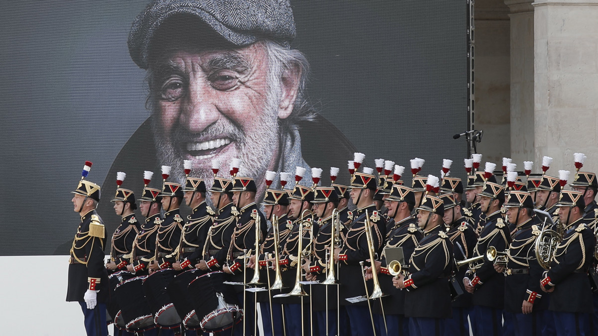 A francia köztársasági őrség zenekara Jean-Paul Belmondo francia színészt ábrázoló kép előtt áll a színész állami gyászszertartásán a párizsi Invalidusok díszudvarán 2021. szeptember 9-én. A színész szeptember 6-án, 88 éves korában hunyt el.