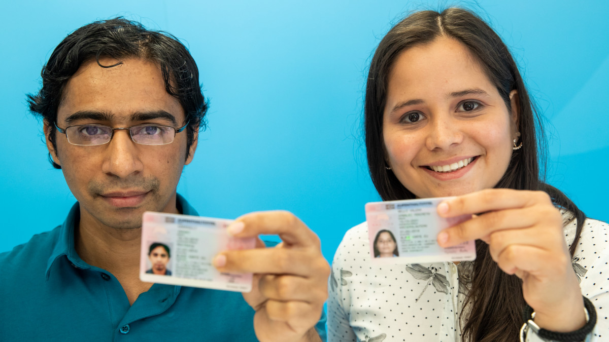 05 July 2018, Nuernberg, Germany: Hymalai Bello, electrical engineer from Venezuela, and Vasant Karasulli, software developer from India hold their Blue card for foreign skilled workers in the Federal Office for Migration and Refugees (Bamf). Nearly 77,000 highly qualified immigrants from non-EU countries have so far been able to work with a so-called Blue Card in Germany. Much of it in highly sought-after occupations - such as an engineer, natural scientist, computer scientist or doctor. (ATTENTION: Parts of the image have been rendered unrecognizable for privacy reasons) Photo: Daniel Karmann/dpa (Photo by Daniel Karmann/picture alliance via Getty Images)