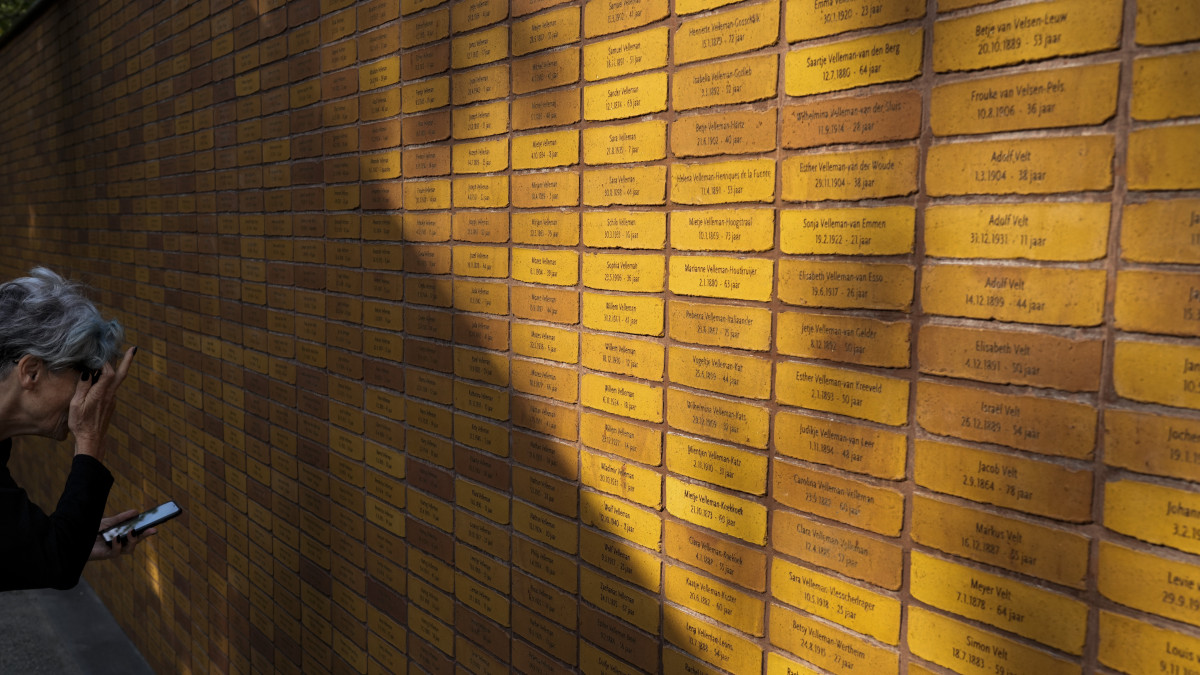 Nevet keres egy nő az új amszterdami holokauszt-emlékmű egyik falán az avatási ünnepségen a holland nagyváros zsidó negyedében 2021. szeptember 19-én. A Daniel Libeskind lengyel származású amerikai építész tervezte alkotás 102 ezer téglája a második világháborús náci német népirtás egy-egy holland zsidó, roma és szinti áldozatának nevét viseli, további ezer, felirat nélküli kő pedig az ismeretlen meggyilkoltakra emlékeztet.
