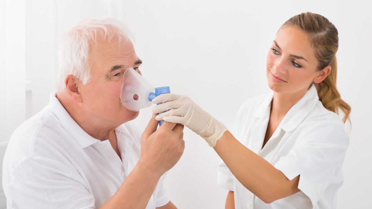 Female Doctor Looking At Senior Male Patient Inhaling Through Oxygen Mask