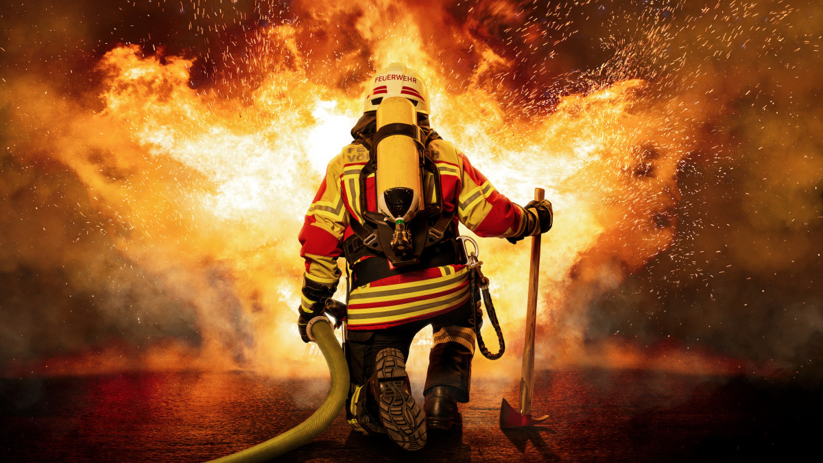Ein Feuerwehrmann steht vor einer groĂen Aufgabe. Er ist mit schwerem Atemschutz ausgerĂźstet und trĂ¤gt eine SchutzausrĂźstung, die ihn vor der Hitze und den Flammen schĂźtzt.