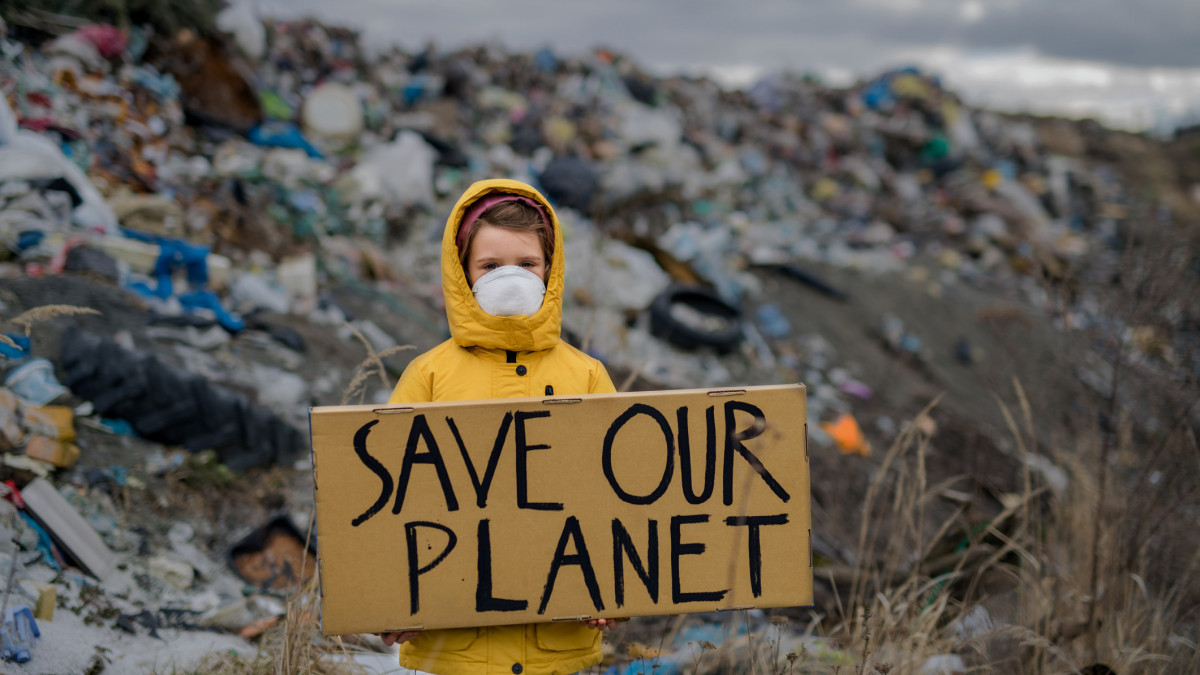 Front view of small child holding placard poster on landfill, environmental pollution concept.