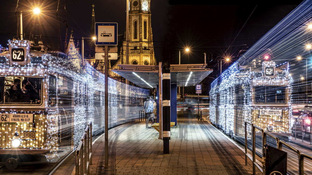 Budapest, 2021. december 11. A Budapesti Közlekedési Központ (BKK) 62A vonalán közlekedő karácsonyi, adventi fényfüzérrel feldíszített villamosok Kőbányán a Szent László téri megállóban. A háttérben 1900-ban felszentelt Lechner Ödön által tervezett neogótikus, eklektikus stílusban épült Szent László-templom esti kivilágításban. Többszörös expozícióval készült felvétel. MTVA/Bizományosi: Róka László