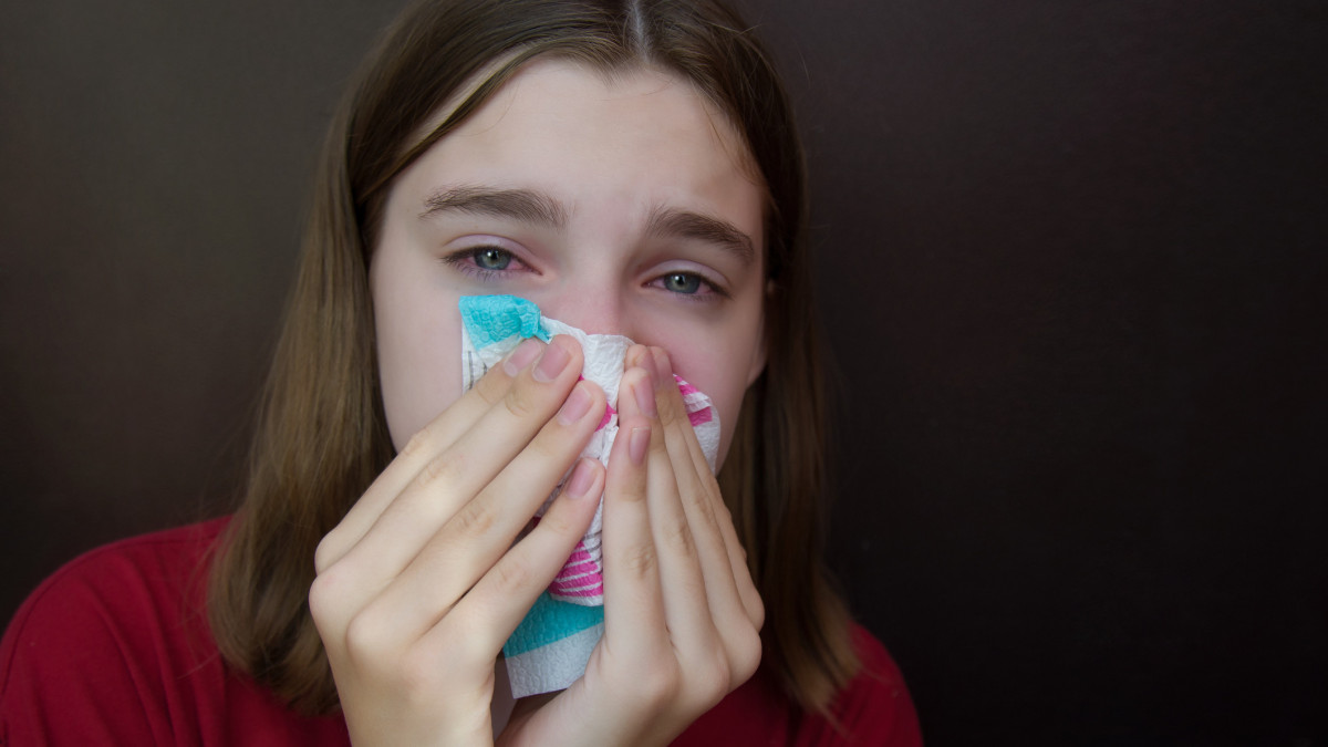 A young girl with an allergy and with red eyes blows her nose in a napkin. Copyspace.