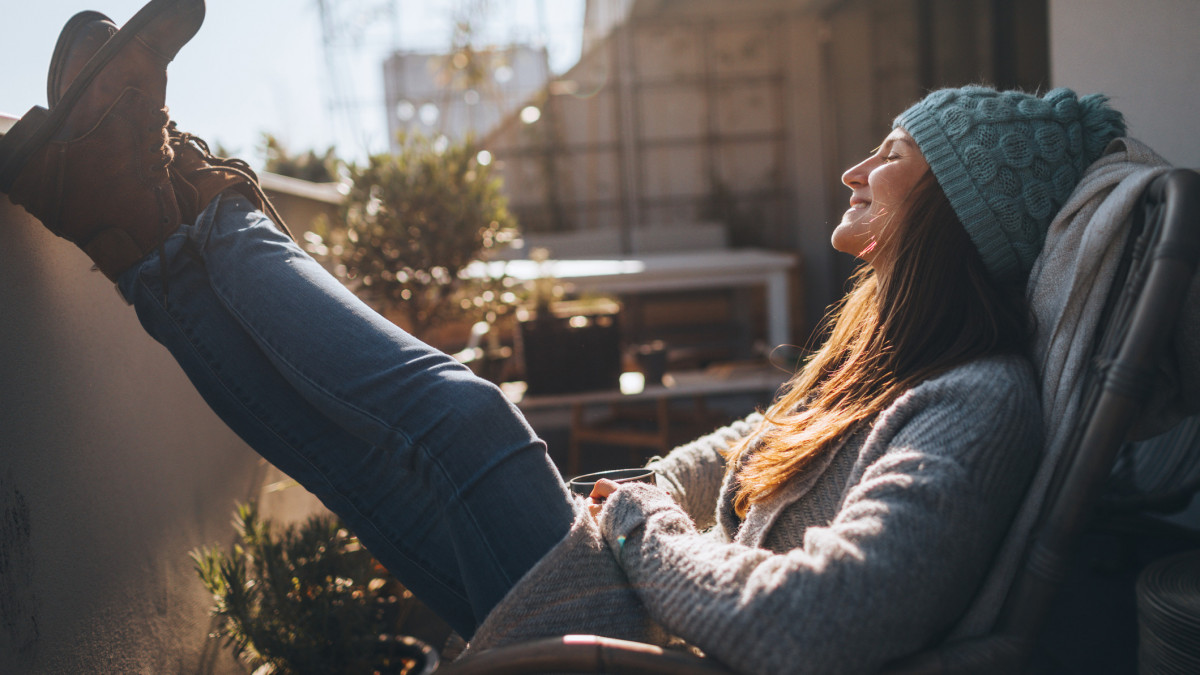 Photo of a young woman taking a few minutes off to relax on the balcony over the city, on a beautiful, sunny, autumn day