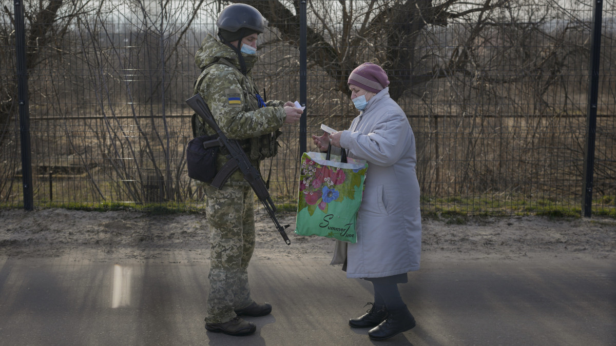 Ukrán katona ellenőrzi az okmányait egy asszonynak, aki az oroszbarát szeparatisták ellenőrzése alatt álló területről az ukrán erők által ellenőrzött területre érkezett a kelet-ukrajnai Sztanicja Luhanszkában, az egyetlen, nappal is nyitva tartó átkelőhelyen 2022. február 22-én.