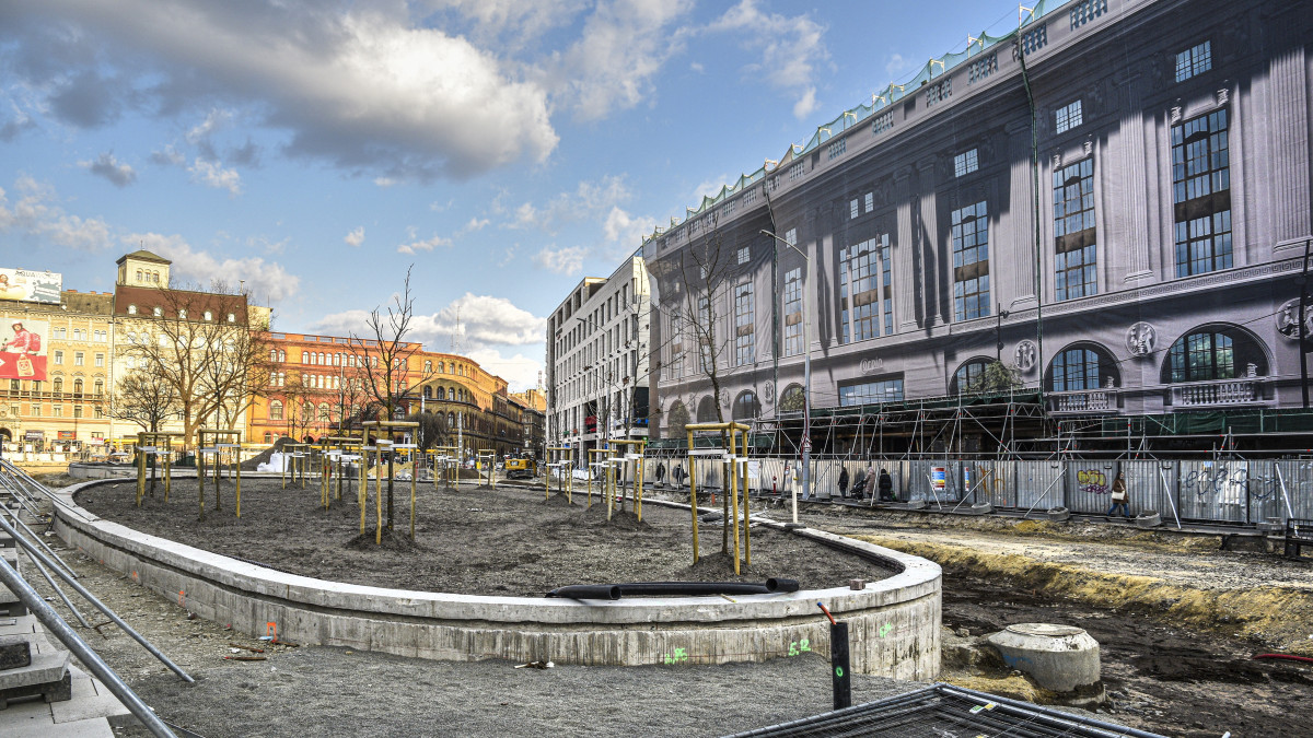 Budapest, 2022. március 8. A felújítás alatt lévő Blaha Lujza tér frissen ültetett fákkal, amely ötvenöt év után új, igényes karaktert kap, egységes arculatú, a mai városi használati igényeket kielégítő belvárosi közösségi térré alakul teraszokkal, találkozóhelyekkel és zöld szigetekkel, kellemes közlekedő környezettel. Jobbra a szintén megújuló, erdetileg 1926-ban megnyitott Corvin Áruház és mögötte az Europeum Bevásárlóközpont épülete. MTVA/Bizományosi: Róka László