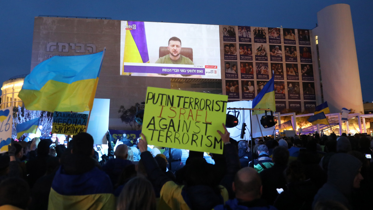 Élőben közvetítik, amint Volodimir Zelenszkij ukrán elnök (a kivetítőn) videoösszeköttetésen keresztül beszél az Ukrajnát ért orosz támadásról az izraeli parlament és a kormány tagjaihoz Tel-Avivban 2022. március 20-án. Vlagyimir Putyin orosz elnök február 24-én rendelte el katonai művelet végrehajtását Ukrajnában.