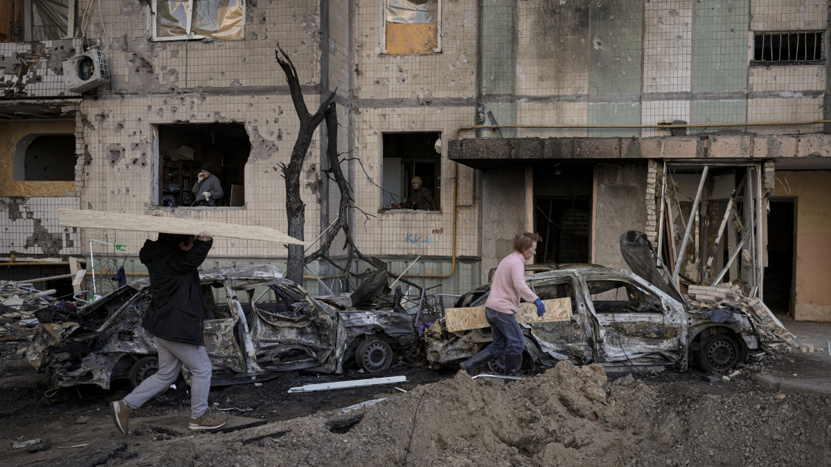 Ablakok bedeszkázásához szükséges faanyagot szállítanak emberek egy bombatalálatban megrongálódott lakóházba Kijevben 2022. március 21-én. Vlagyimir Putyin orosz elnök február 24-én rendelte el katonai művelet végrehajtását Ukrajnában.