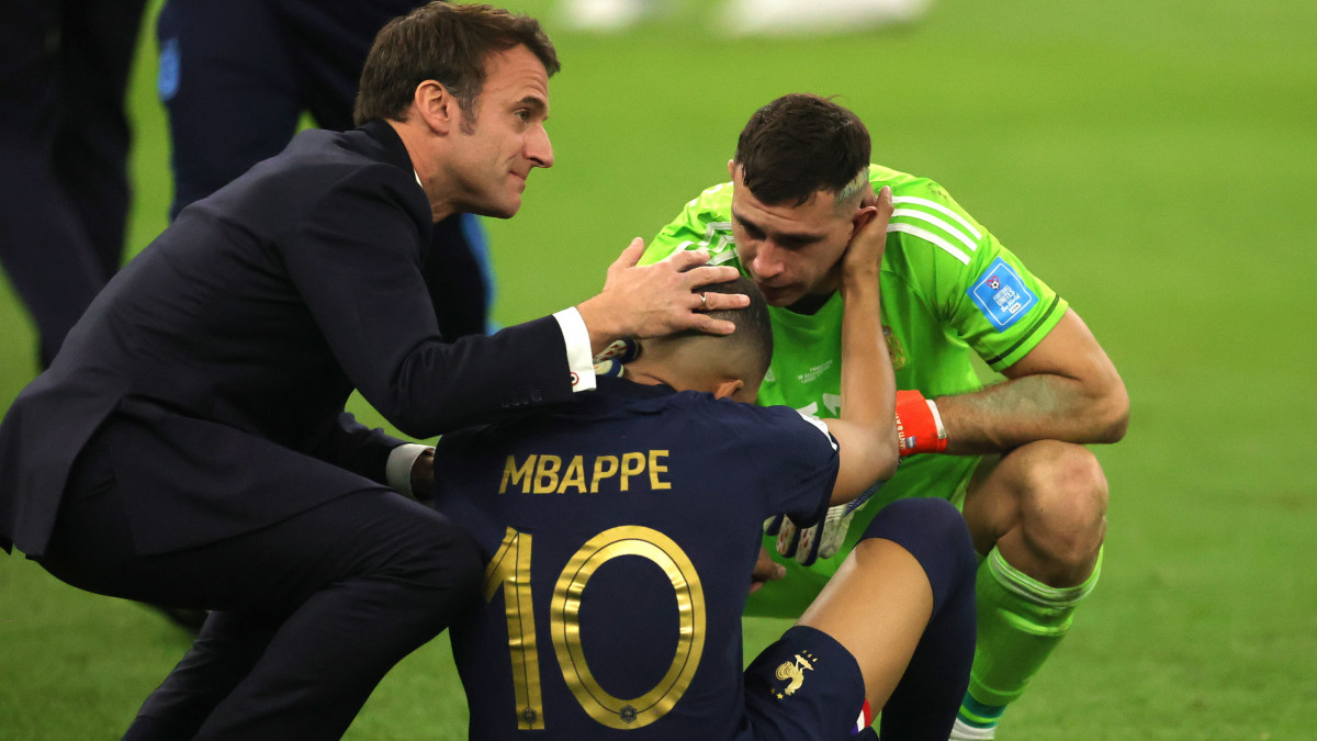 A francia Kylian Mbappét (k) Emiliano Martínez argentin kapus (j) és Emmanuel Macron francia elnök vigasztalja, miután a franciák 4-2-re kikaptak a katari labdarúgó-világbajnokság döntőjében játszott Argentína-Franciaország mérkőzés 3-3-as hosszabbítása utáni tizenegyes-párbajban a Loszaíl Stadionban 2022. december 18-án.